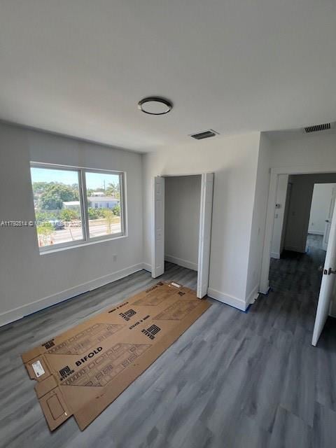 unfurnished bedroom featuring baseboards, a closet, wood finished floors, and visible vents