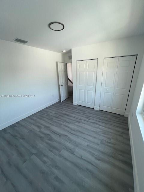 unfurnished bedroom featuring two closets, baseboards, visible vents, and wood finished floors