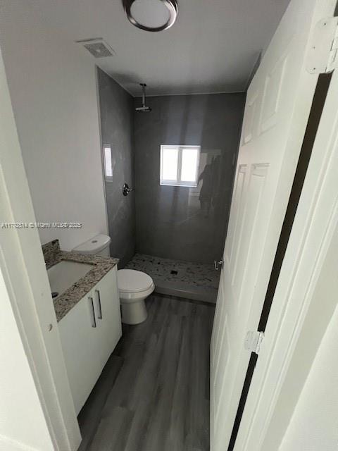 bathroom with vanity, visible vents, wood finished floors, toilet, and a shower stall