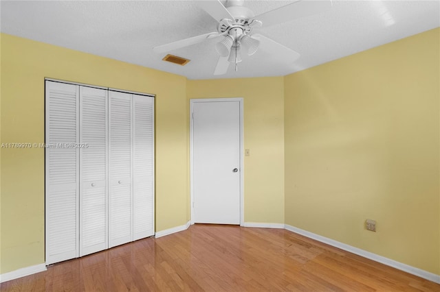 unfurnished bedroom with baseboards, visible vents, wood finished floors, and a closet