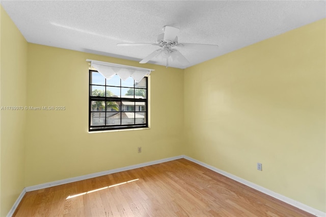 spare room featuring baseboards, light wood finished floors, and a textured ceiling