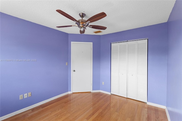 unfurnished bedroom featuring baseboards, a textured ceiling, wood finished floors, and a closet