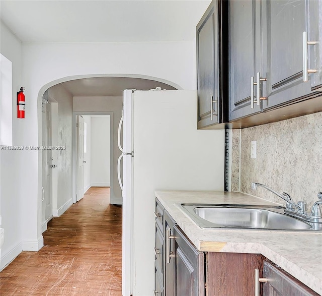 kitchen with light countertops, arched walkways, a sink, light wood-style flooring, and backsplash