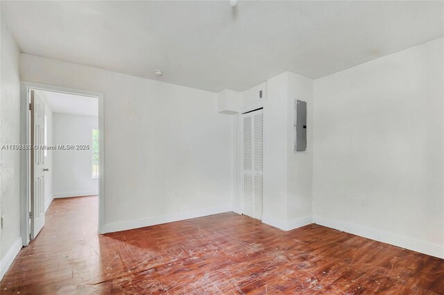 unfurnished room with baseboards, wood finished floors, and electric panel