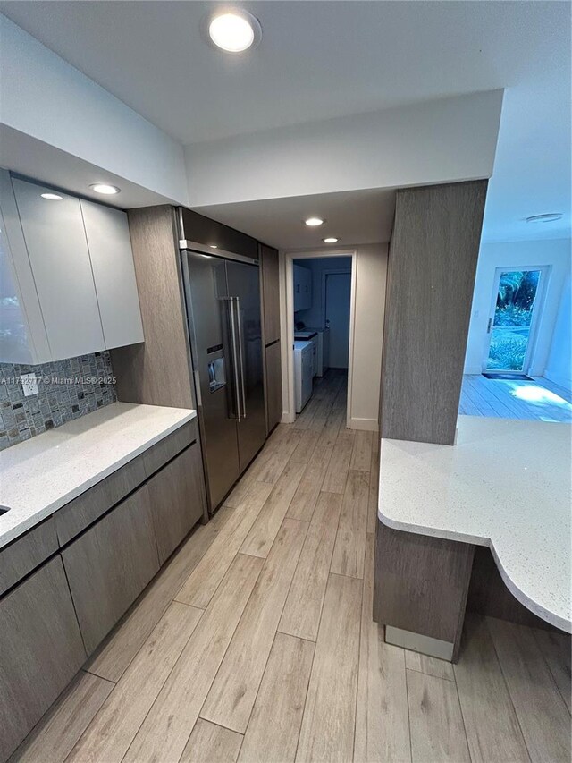 kitchen featuring washing machine and dryer, light wood-type flooring, light countertops, built in refrigerator, and backsplash