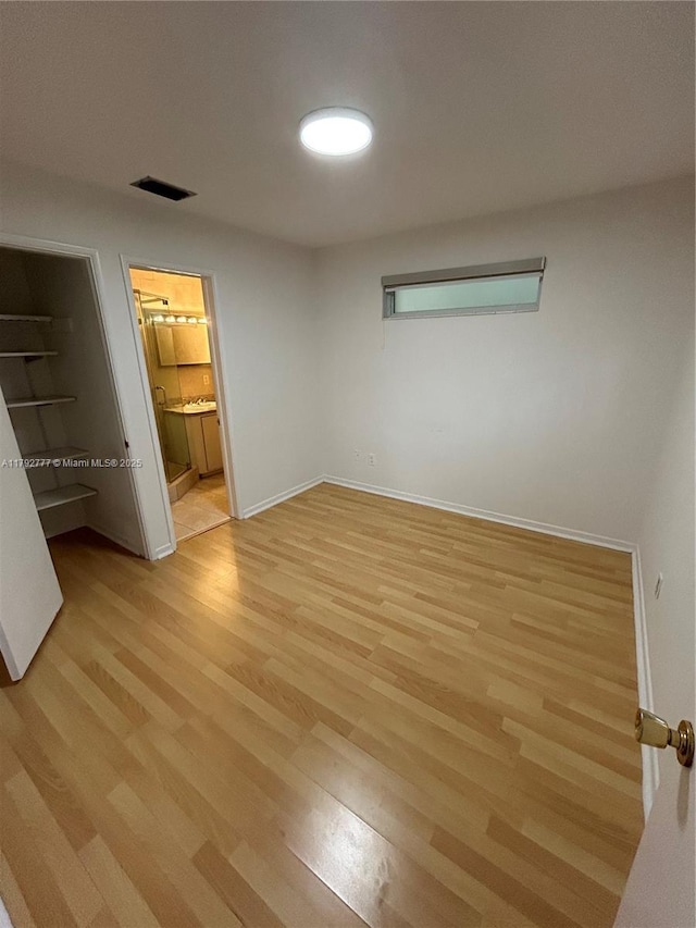 unfurnished bedroom featuring a walk in closet, visible vents, baseboards, light wood-style floors, and ensuite bath