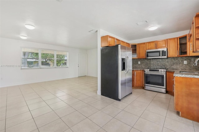 kitchen with brown cabinetry, a sink, decorative backsplash, and appliances with stainless steel finishes