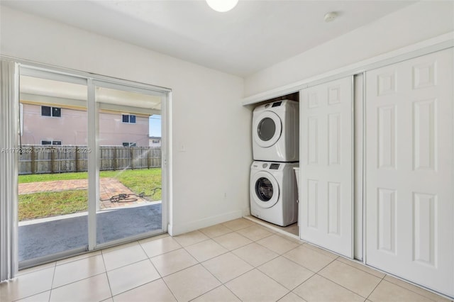 laundry room with light tile patterned flooring, stacked washer / drying machine, baseboards, and laundry area