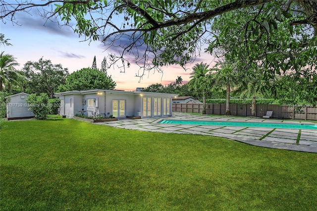 pool at dusk with a yard, a fenced in pool, a fenced backyard, and a patio area