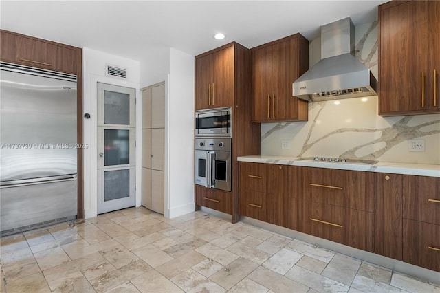 kitchen with light countertops, built in appliances, wall chimney exhaust hood, and visible vents