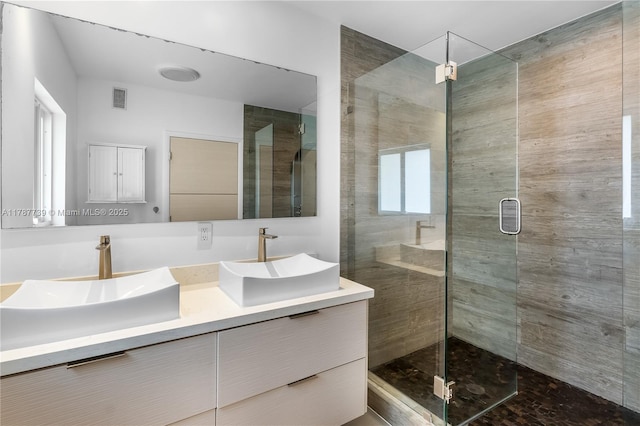 full bath featuring visible vents, a sink, double vanity, and a shower stall