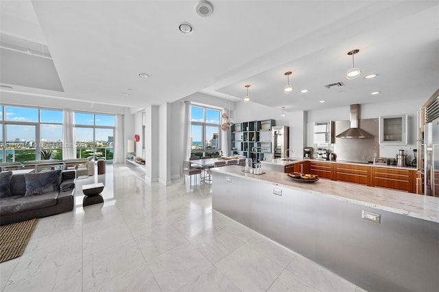 interior space featuring light stone countertops, open floor plan, recessed lighting, wall chimney exhaust hood, and brown cabinets