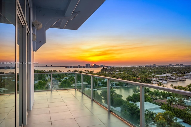 balcony at dusk featuring a water view and a view of city