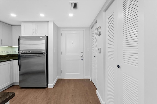 kitchen featuring visible vents, freestanding refrigerator, wood finished floors, dark countertops, and white cabinetry