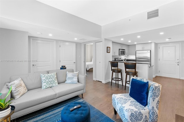 living room featuring baseboards, recessed lighting, wood finished floors, and visible vents