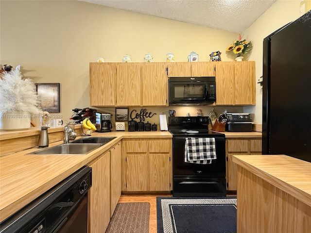 kitchen with light brown cabinetry, a textured ceiling, a sink, black appliances, and vaulted ceiling