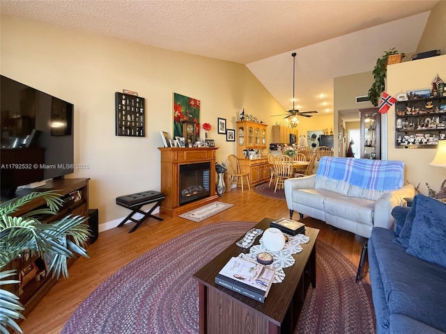 living area featuring a glass covered fireplace, a ceiling fan, wood finished floors, and lofted ceiling