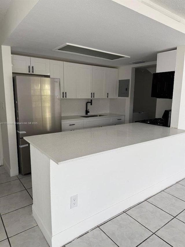 kitchen with electric panel, a sink, light tile patterned floors, white cabinets, and freestanding refrigerator