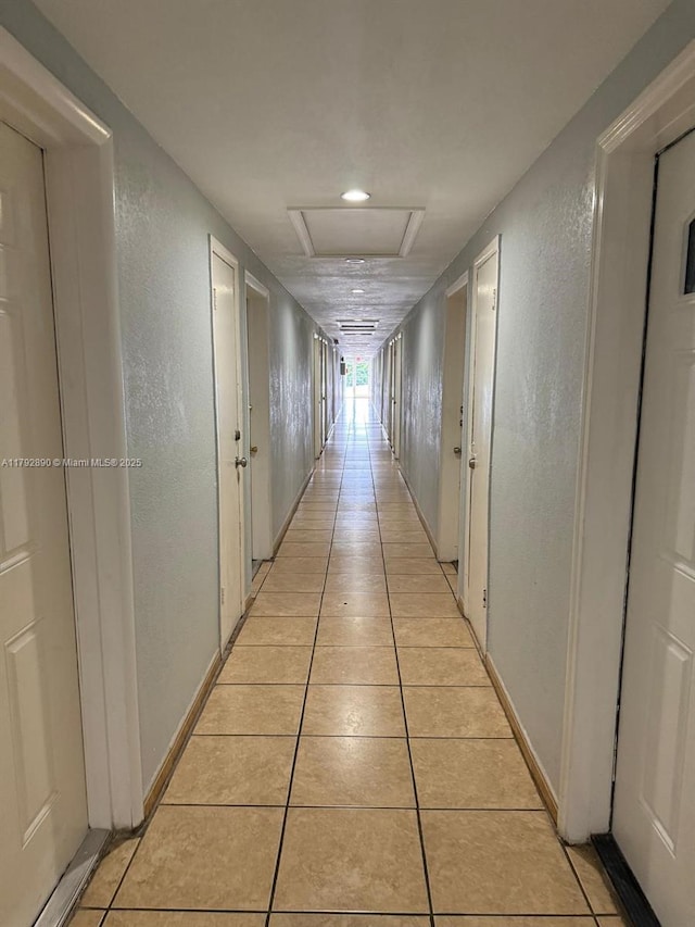hallway featuring attic access, a textured wall, and light tile patterned flooring