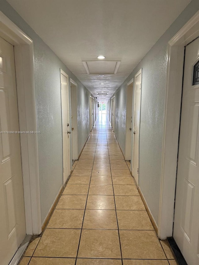 hallway featuring attic access, a textured wall, and light tile patterned flooring