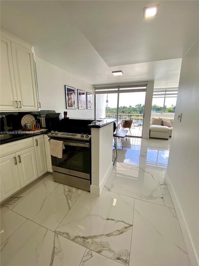 1700 NW N River Dr Unit 501, Miami, FL 33125 - kitchen featuring marble finish floor, a peninsula, baseboards, white cabinetry, and stainless steel electric stove