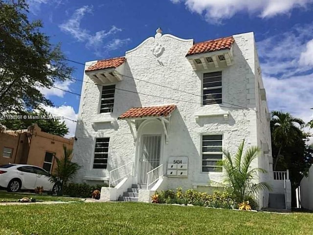 mediterranean / spanish-style house featuring a tile roof, a front yard, and stucco siding