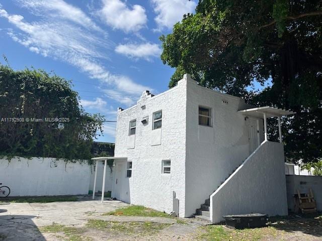 back of house featuring stucco siding, fence, and stairs