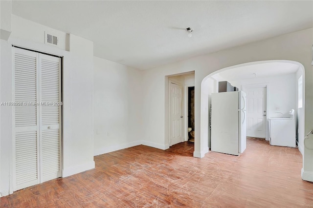unfurnished bedroom featuring visible vents, arched walkways, baseboards, freestanding refrigerator, and washer / dryer