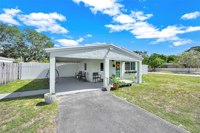 bungalow-style home featuring fence private yard, a front lawn, stucco siding, a porch, and a carport