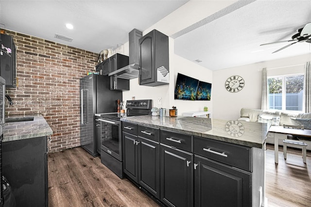 kitchen with dark cabinets, a peninsula, range with electric cooktop, and brick wall