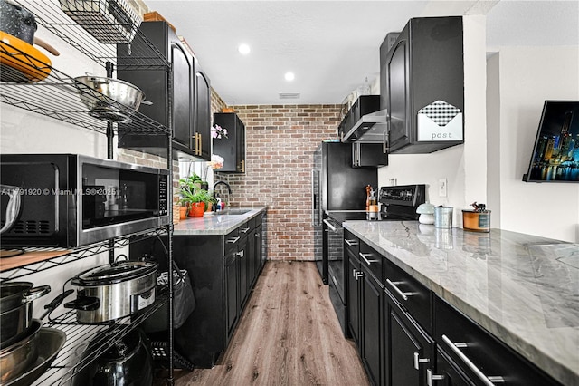 kitchen featuring black electric range, dark cabinetry, light wood-style floors, and brick wall