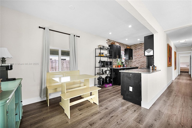 kitchen featuring dark cabinetry, a peninsula, wood finished floors, and light countertops