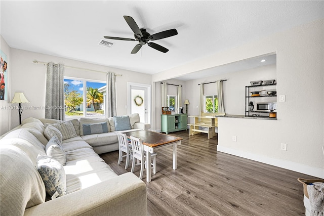 living room with a ceiling fan, baseboards, visible vents, and dark wood-style floors