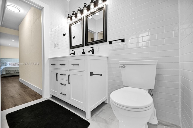 bathroom with toilet, ensuite bath, tile walls, and vanity