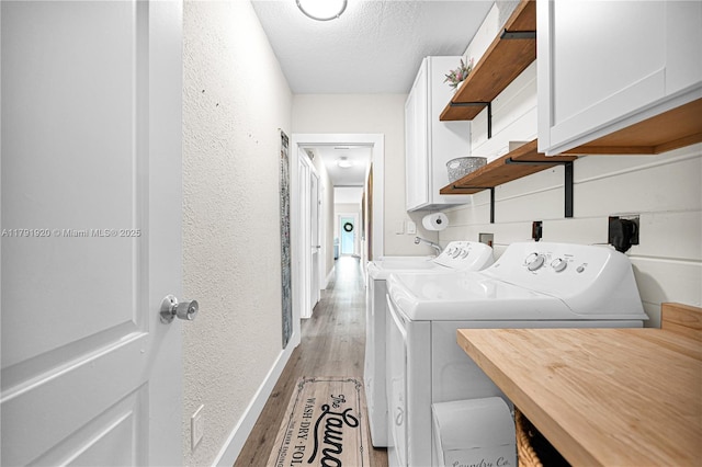laundry room featuring a textured ceiling, cabinet space, baseboards, separate washer and dryer, and a textured wall
