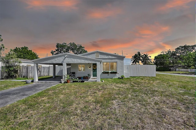 view of front of house with fence, stucco siding, a front yard, a carport, and driveway