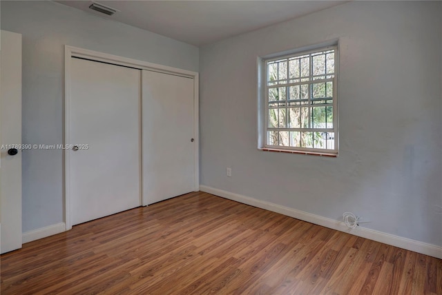 unfurnished bedroom featuring baseboards, a closet, wood finished floors, and visible vents