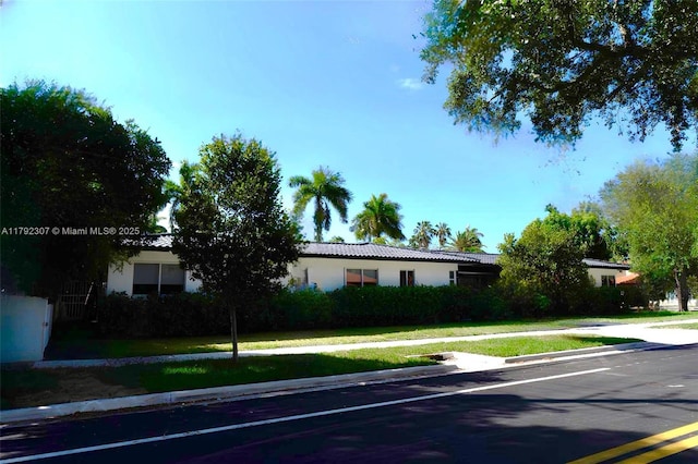 ranch-style house featuring a front lawn, stucco siding, and a tile roof