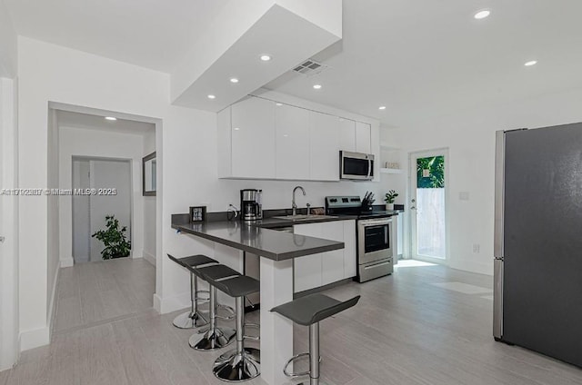 kitchen featuring a breakfast bar area, modern cabinets, white cabinetry, dark countertops, and appliances with stainless steel finishes