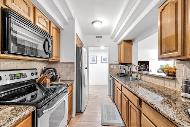 kitchen featuring backsplash, light stone countertops, a sink, light wood-style floors, and stainless steel appliances