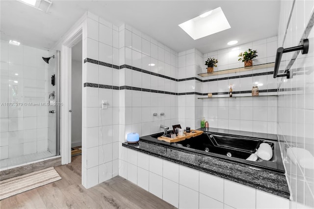 full bath with tile walls, a tub with jets, wood finished floors, a skylight, and a stall shower