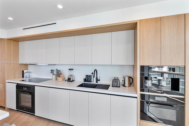 2127 Brickell Ave Unit 2704, Miami, FL 33129 - kitchen with a sink, light countertops, black appliances, light wood-style floors, and white cabinetry
