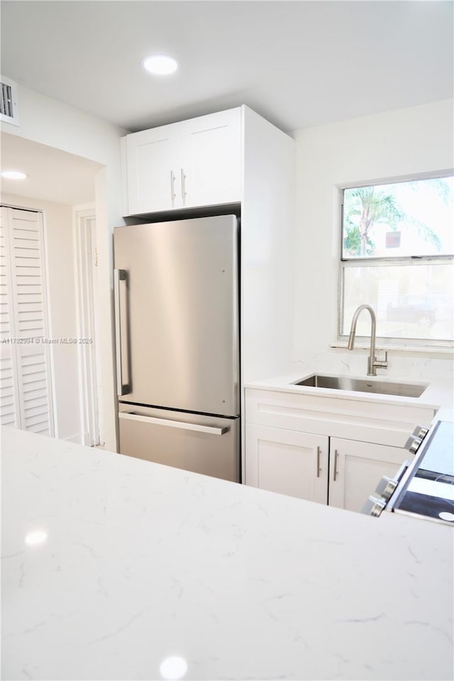 kitchen with white cabinets, light stone counters, a sink, freestanding refrigerator, and recessed lighting