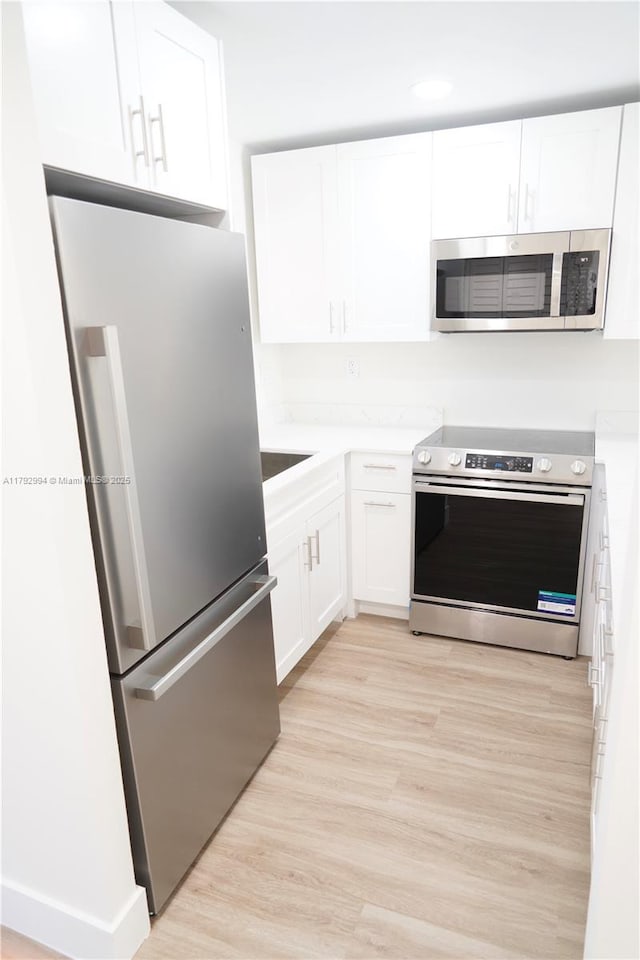 kitchen with white cabinets, stainless steel appliances, light countertops, and light wood-style floors