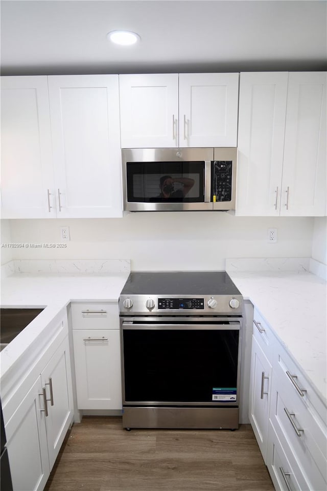 kitchen with white cabinets, light stone countertops, appliances with stainless steel finishes, recessed lighting, and wood finished floors