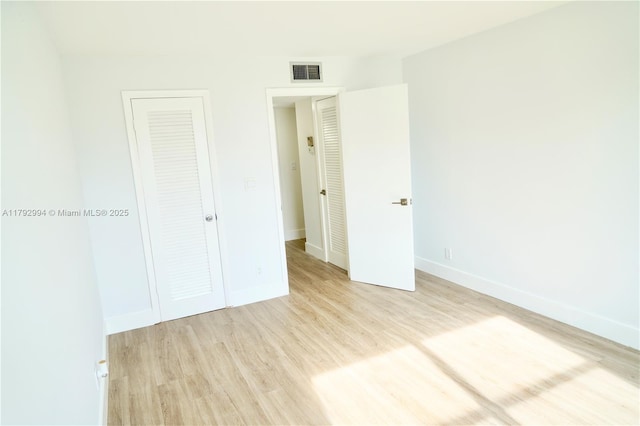 unfurnished bedroom with visible vents, light wood finished floors, baseboards, and a closet