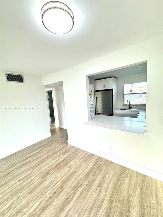 unfurnished living room featuring visible vents, a sink, baseboards, and wood finished floors