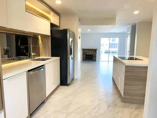 kitchen with white cabinets, a fireplace, light countertops, stainless steel appliances, and modern cabinets
