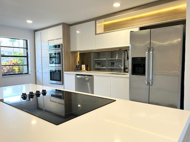 kitchen with appliances with stainless steel finishes, a sink, light countertops, white cabinetry, and modern cabinets