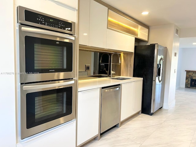 kitchen with white cabinets, appliances with stainless steel finishes, a sink, light countertops, and visible vents